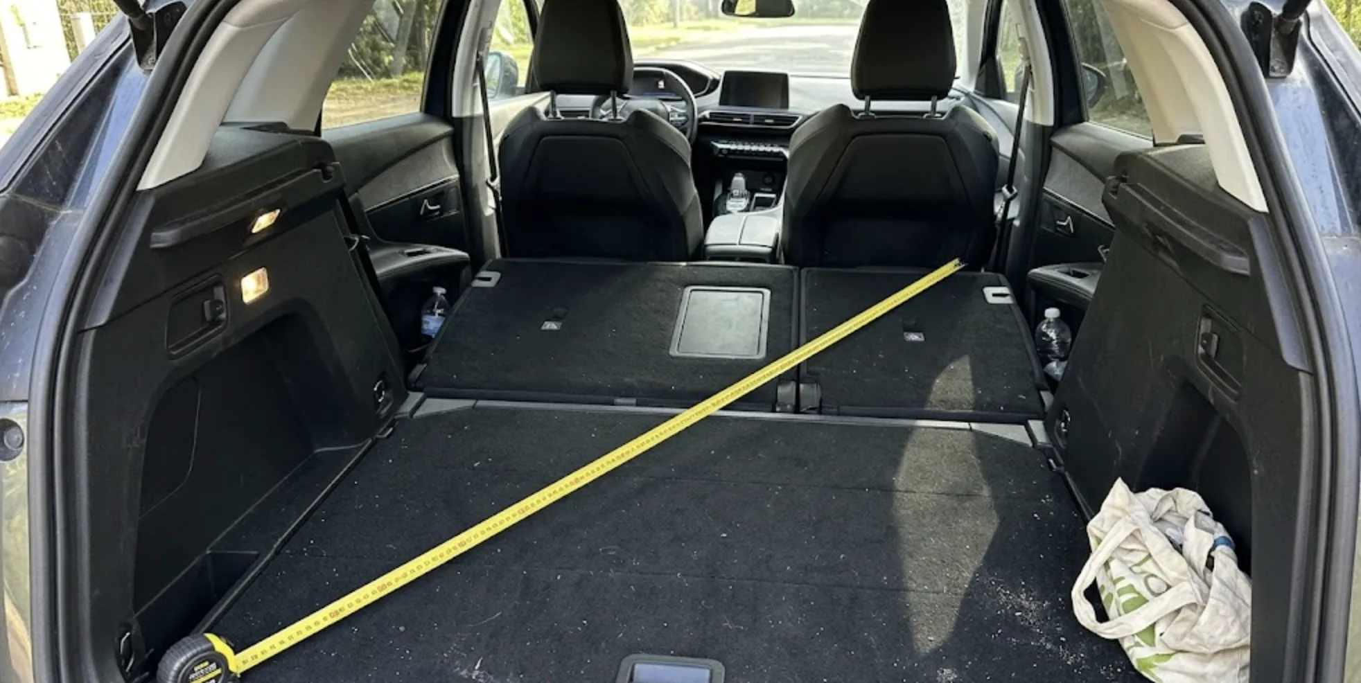 Vue intérieure du coffre d'un Peugeot 3008 avec les sièges complètement rabattus et un mètre ruban jaune étiré sur le plancher sombre — test de longueur disponible
