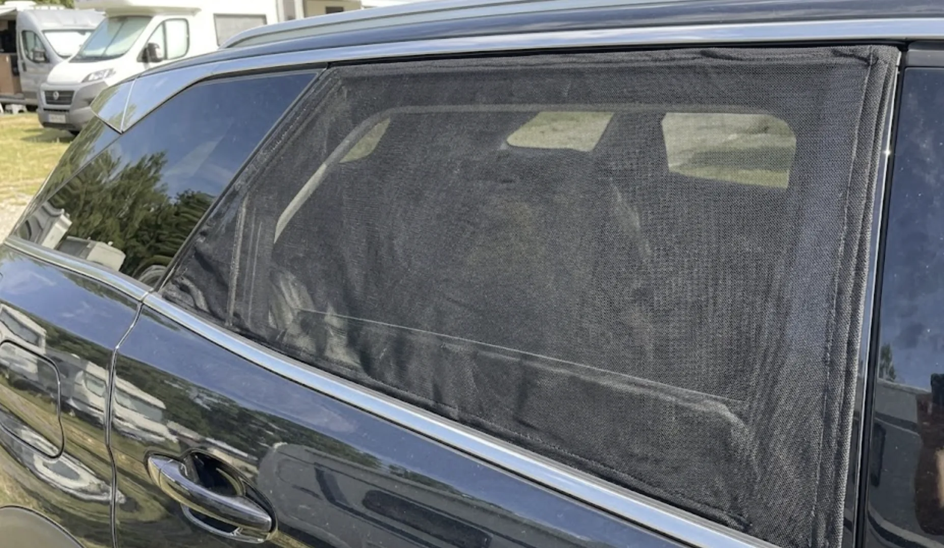 Gros plan extérieur sur la vitre arrière d'une voiture recouverte d'une chaussette en maille noire anti-moustiques, la vitre légèrement abaissée de 3 centimètres en dessous — astuce bivouac voiture